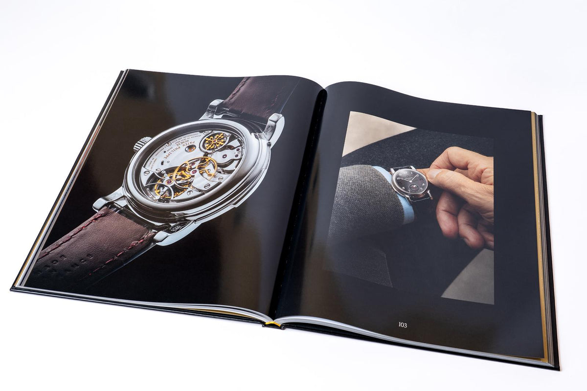 An open book featuring a watch movement and a watch held in a collector’s hand